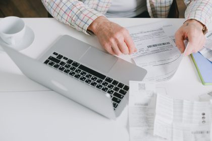 Mãos organizam documentos sobre uma mesa diante de um laptop.