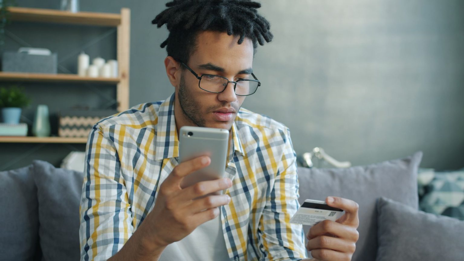 Homem usa um smartphone e um cartão de crédito enquanto faz uma compra online em casa.