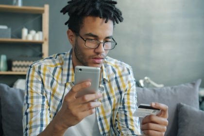Homem usa um smartphone e um cartão de crédito enquanto faz uma compra online em casa.