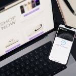 Laptop e smartphone sobre uma mesa, exibindo páginas de compras online e uma interface de pagamento digital.
