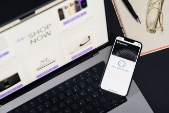 Laptop e smartphone sobre uma mesa, exibindo páginas de compras online e uma interface de pagamento digital.