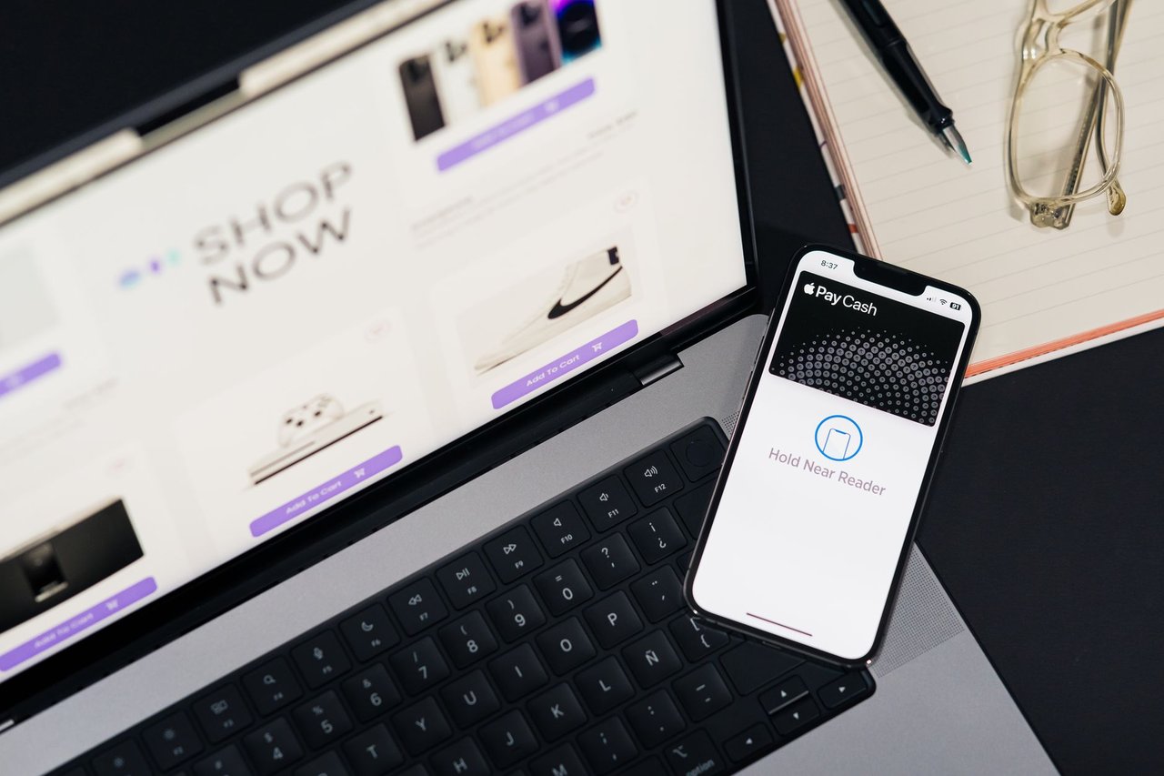 Laptop e smartphone sobre uma mesa, exibindo páginas de compras online e uma interface de pagamento digital.