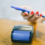 Mão aproxima um smartphone de um terminal de pagamento para realizar uma transação sem contato.